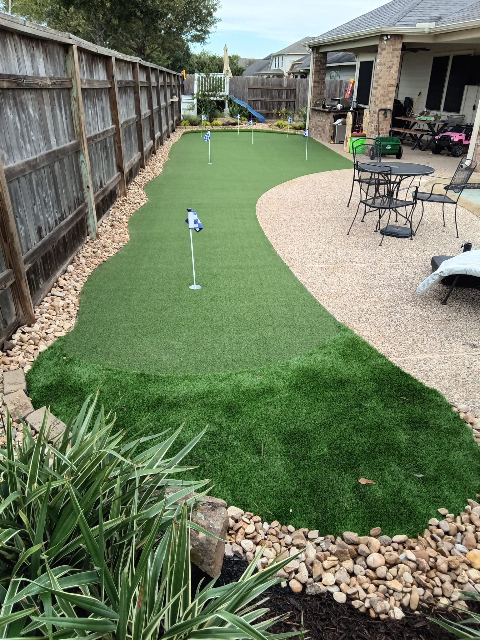 Backyard putting green with river rock border and patio seating area